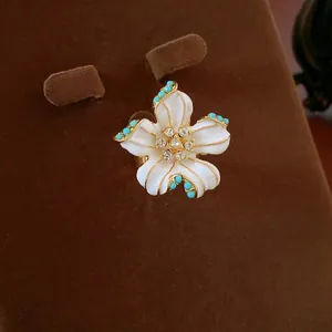 Detailed close-up of an elegant white enamel flower jewelry piece with zircon and turquoise beads