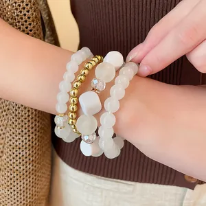 Close-up detail of bohemian white acrylic and gold bead bracelet set worn on wrist