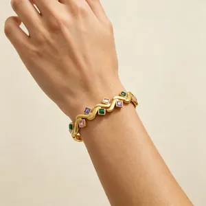 Detailansicht eines vergoldeten Armbands mit bunten quadratischen Edelsteinen am Handgelenk.