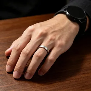 Close-up view of a minimalist brushed titanium steel ring worn on a hand over a wooden table