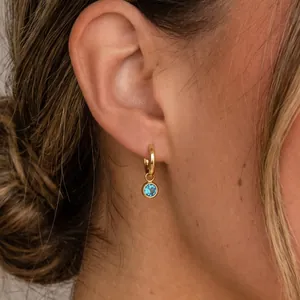Détail d'une boucle d'oreille en acier titane doré avec un zircon bleu brillant.