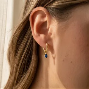 Gros plan de créoles dorées avec un pendentif en zircone bleu foncé en forme de poire