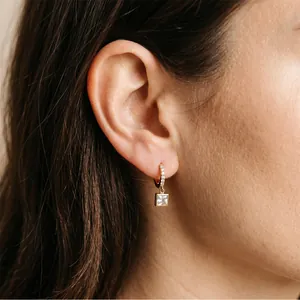 Gros plan de créoles dorées élégantes avec un pendentif étincelant en zircon de forme carrée