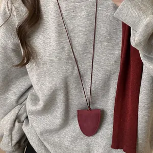 Vue détaillée d'un collier pochette en cuir bordeaux porté sur un sweat-shirt gris