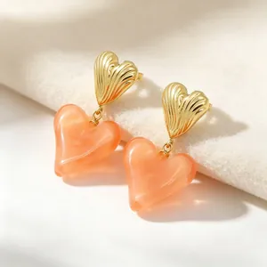 Gros plan de boucles d'oreilles pendantes cœur en métal doré et résine pêche.