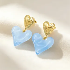 Vue macro de boucles d'oreilles cœur en résine marbrée bleue et métal doré nervuré