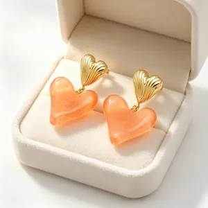 Détail de boucles d'oreilles cœur dorées avec pendentifs cœur en résine pêche en boîte