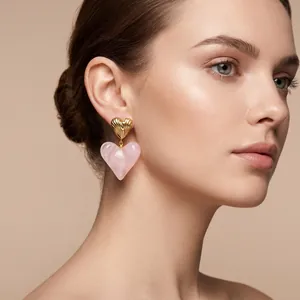 Vue détaillée de boucles d'oreilles cœur rose avec métal doré texturé portées par mannequin