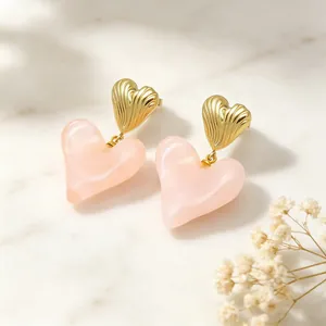 Détail de boucles d'oreilles cœur en métal doré et résine rose sur marbre blanc