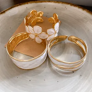 Elegante roestvrijstalen open armbanden met witte emaille bloemen en texturen.