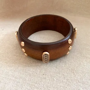Detailansicht eines Vintage-Holzarmreifens mit goldfarbenen Nieten und geometrischen Mustern.