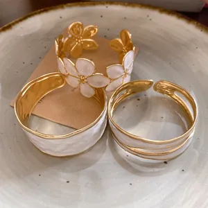 Detailopname van drie elegante wit geëmailleerde gouden open armbanden op een bord