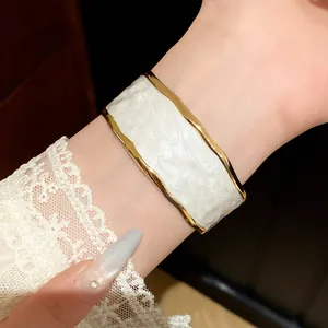 Gedetailleerde weergave van een elegante gouden manchetarmband met wit email op een pols