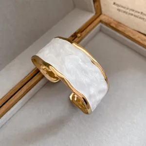 Gedetailleerde opname van wit marmerglazuur op een gouden onregelmatige gegolfde armband