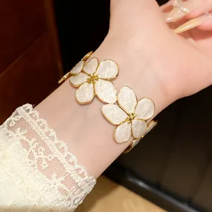 Close-up van een elegante gouden roestvrijstalen armband met witte emaille bloembedeltjes