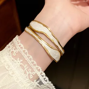 Close-up van een stijlvolle wit geëmailleerde en goudkleurige golvende open manchetarmband.