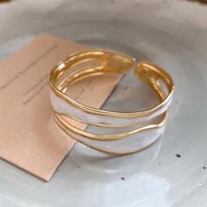 Detailweergave van de golvende witte emaille op een gouden roestvrijstalen armband.
