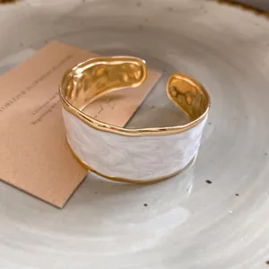 Detail van een golvende gouden roestvrijstalen armband met wit marmeren emaille.