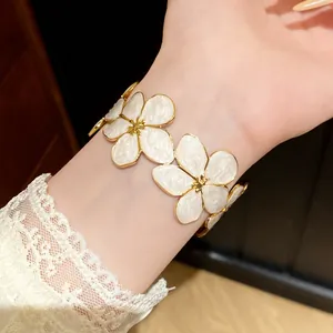 Detailweergave van witte emaille bloemenarmband in goudkleur gedragen met kant aan de pols