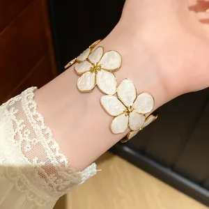 Gedetailleerde close-up van een gouden stalen armband met witte bloemmotieven van email