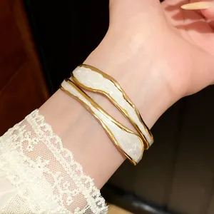 Detailweergave van een elegante gouden roestvrijstalen golfarmband met wit email op de pols