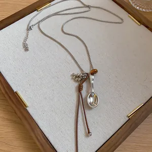 Minimalist long necklace with spoon pendant, leather cord, and resin bead on display tray