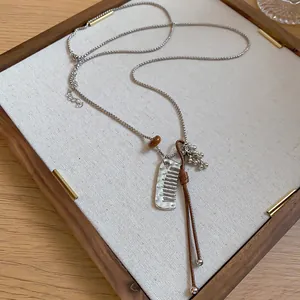 Close-up of a Korean style necklace with a silver comb charm and brown cord on a tray