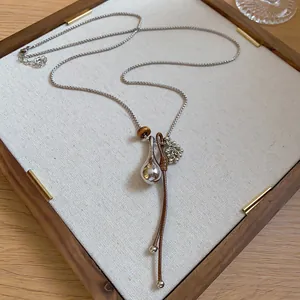 Close-up of a minimalist silver teardrop pendant necklace with brown leather cord.