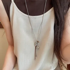Detail of a minimalist long necklace featuring a fish pendant and leather cord detail