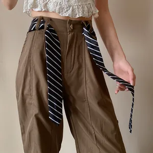 Detalle de pantalones marrones de cintura alta con cinturón de cinta a rayas blancas