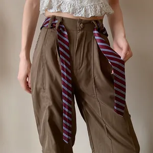Detalle de corbata de rayas rojas usada como cinturón en pantalones marrones de talle alto