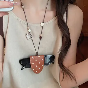 Detailed close-up of a brown polka dot leather sunglasses pouch worn as a necklace