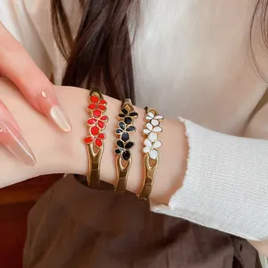 Close-up of vintage enamel flower bangles in red, black, and white on a wrist.