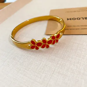 Close-up detail of a vintage gold bangle featuring three vibrant red enamel flowers.