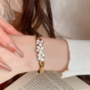 Detailed view of a vintage style gold bangle with white enamel flowers worn on a wrist.