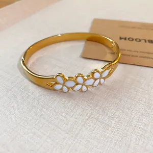 Close-up detail of vintage gold bangle featuring elegant white enamel floral motifs on a textured surface