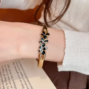 Close-up view of a vintage gold bangle with black enamel flowers worn on a wrist.