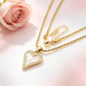Gros plan d'un collier chaîne torsadée dorée avec pendentif cœur en nacre et cristaux