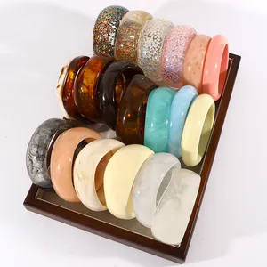 Collection of various vintage marbled resin wide bangles displayed in a wooden tray