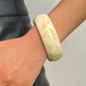 Close-up detail of a wide marbled cream and tan resin bangle worn on a model's wrist