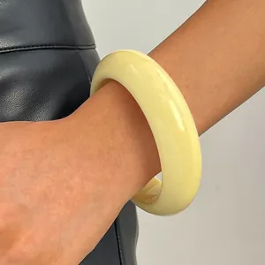 Close-up of a chunky cream resin bangle bracelet worn on a wrist for a retro look.