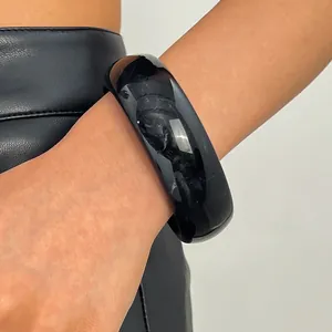 Detail showing a glossy black resin wide bangle bracelet worn on a female wrist for style.
