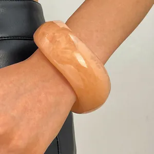 Close-up view of a vintage marbled peach resin wide bangle bracelet on a wrist.