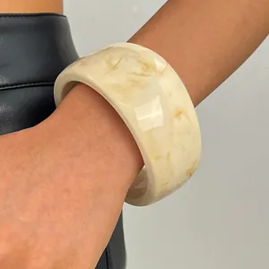 Close-up of a wide marbled resin bangle with amber patterns on a cream base