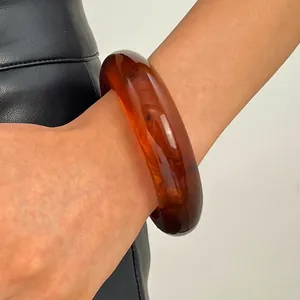 Close-up view of a vintage wide amber resin bangle bracelet worn on a wrist with leather