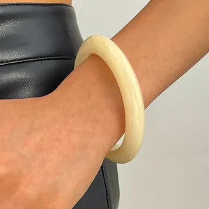 Detailed shot of a chunky retro cream-colored resin bangle worn on a wrist against black leather
