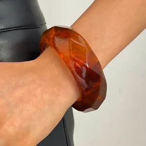 Close-up detail of a vintage amber marbled resin faceted wide bangle on a model's wrist