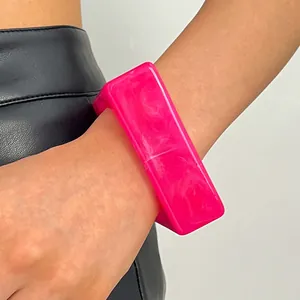 Detailed view of a retro hot pink marbled resin wide bangle bracelet on a model's wrist