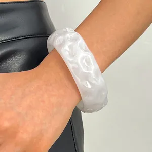 Close-up of a white vintage resin wide bangle with irregular textures on arm.