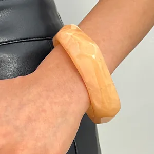 Close-up detail of wide marbled resin bangle with geometric facets in peach color